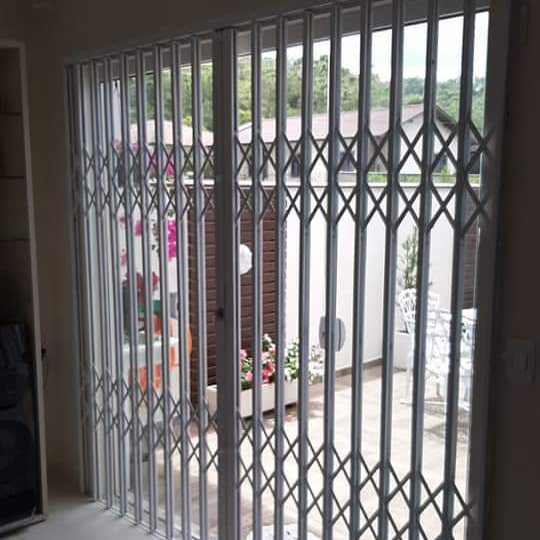 Grade pantográfica branca fechando uma porta de vidro